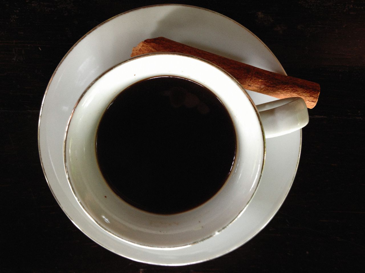 About Top view of a porcelain cup of black coffee with a cinnamon stick on a saucer.