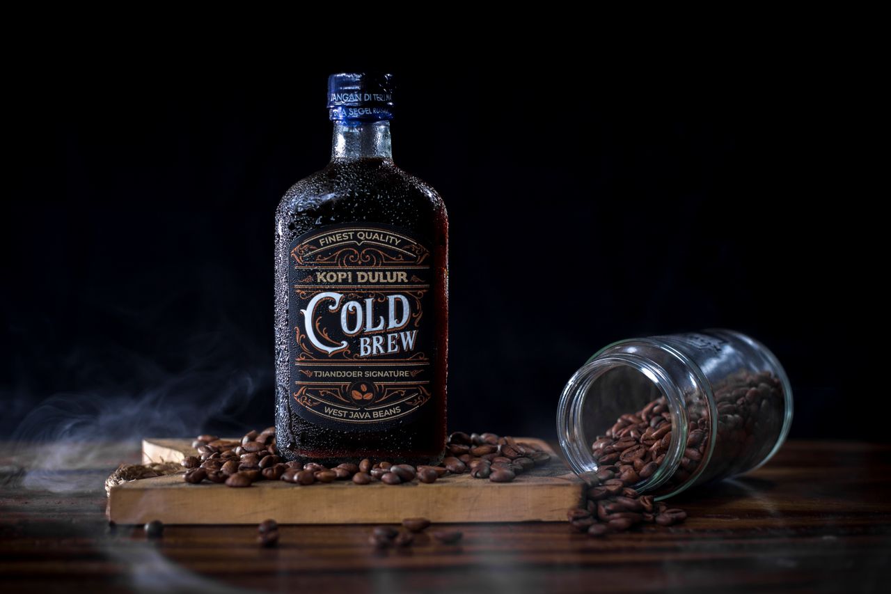 Offerings A cold brew coffee bottle with West Java beans, surrounded by scattered coffee beans.